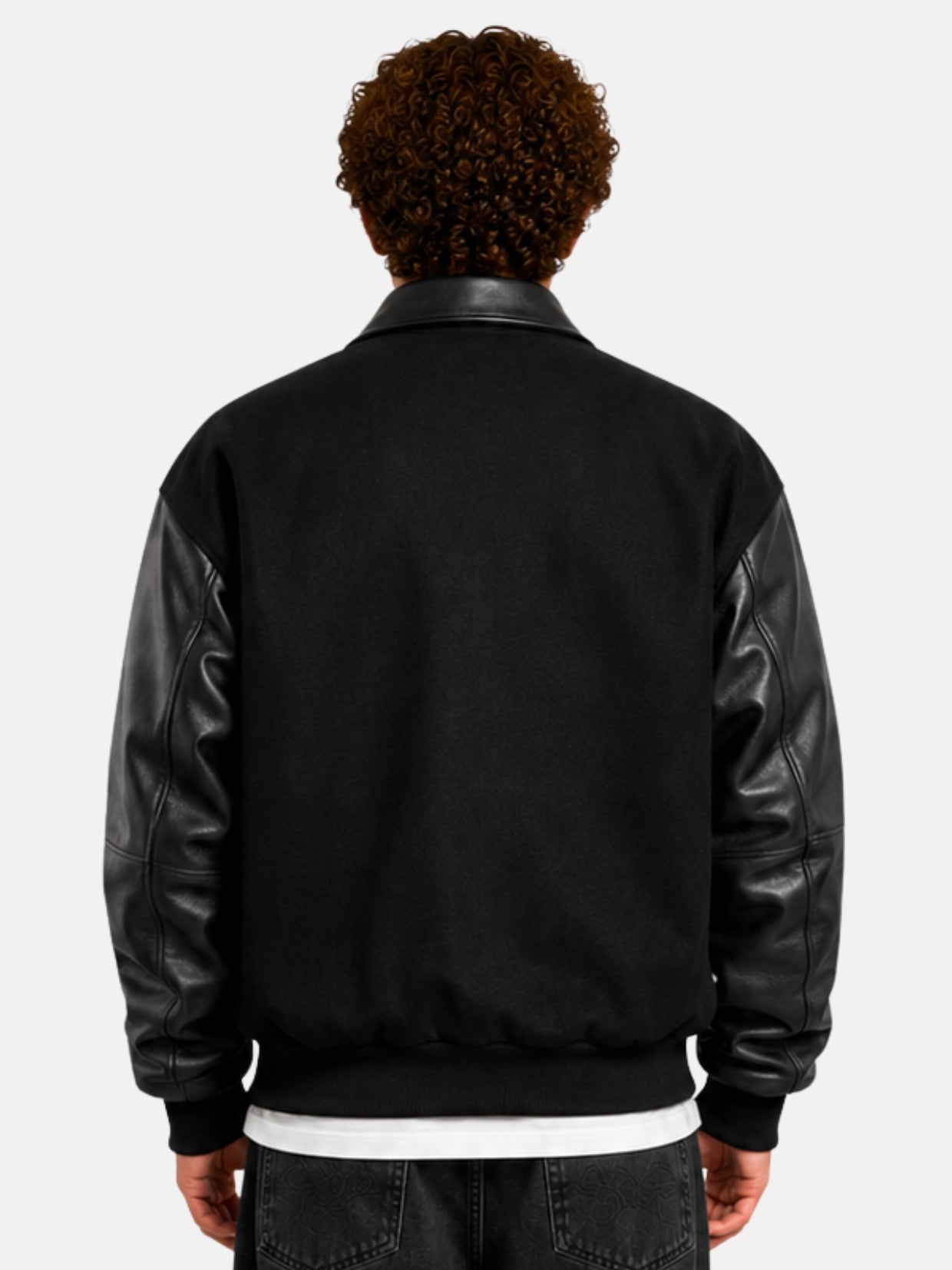 Back view of a black wool varsity jacket with leather sleeves and collar on model