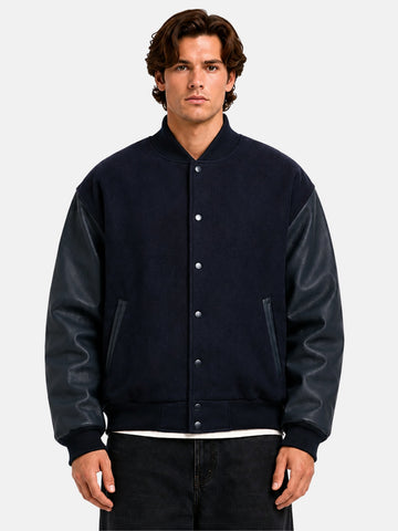 Man wearing a navy blue varsity jacket with leather sleeves and tonal snap front