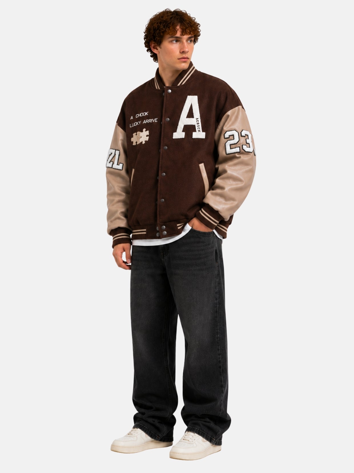 Full-length view of a brown letterman jacket with patches, black jeans and cream sneakers