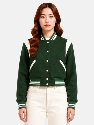 Model wearing forest green wool varsity jacket buttoned to the collar, five cream snaps down the placket, curved cream shoulder panel visible at both collarbones