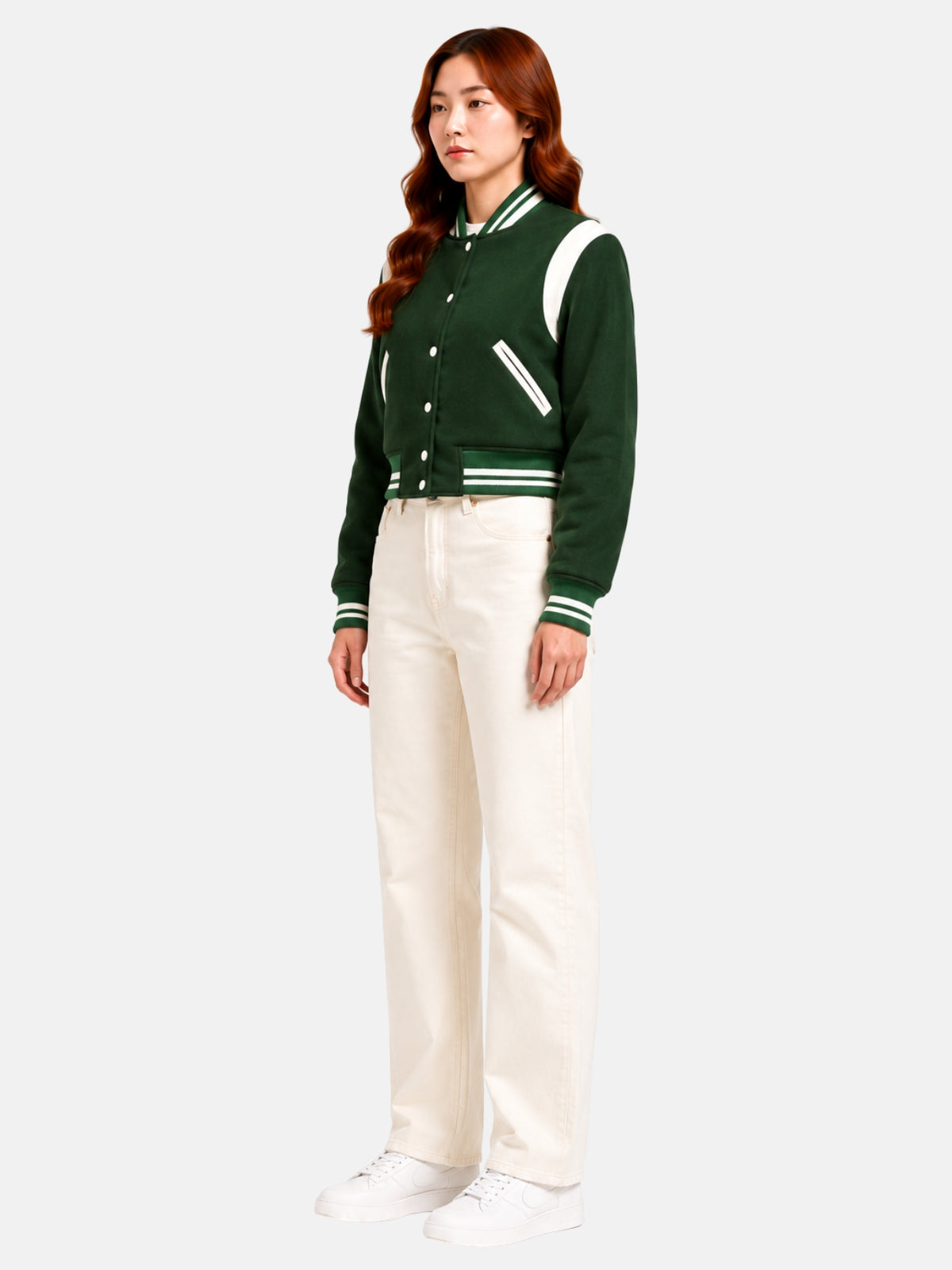 Full-body three-quarter shot of model walking in the forest green wool varsity jacket, cream ribbed waistband and cuffs visible against light denim