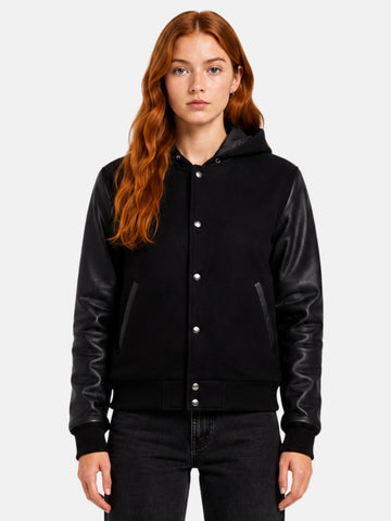 Woman wearing a black hooded varsity jacket with leather sleeves and hood up