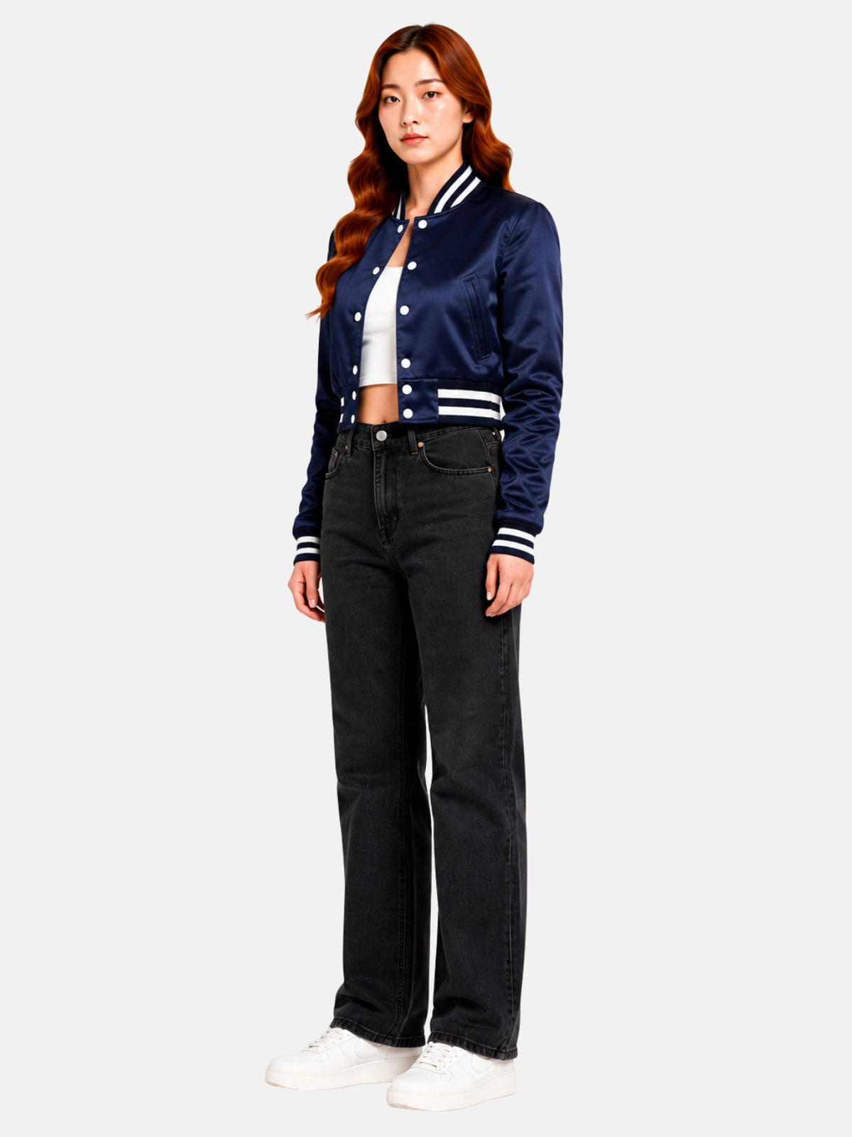 Full-body three-quarter shot of model walking in the cropped satin varsity jacket, white sneakers and black denim