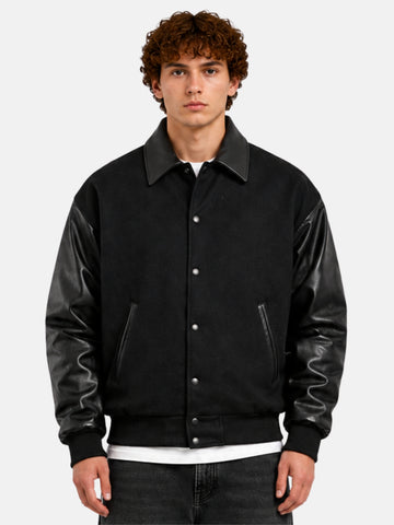 Man wearing an all-black oversized varsity jacket with leather collar and snap front