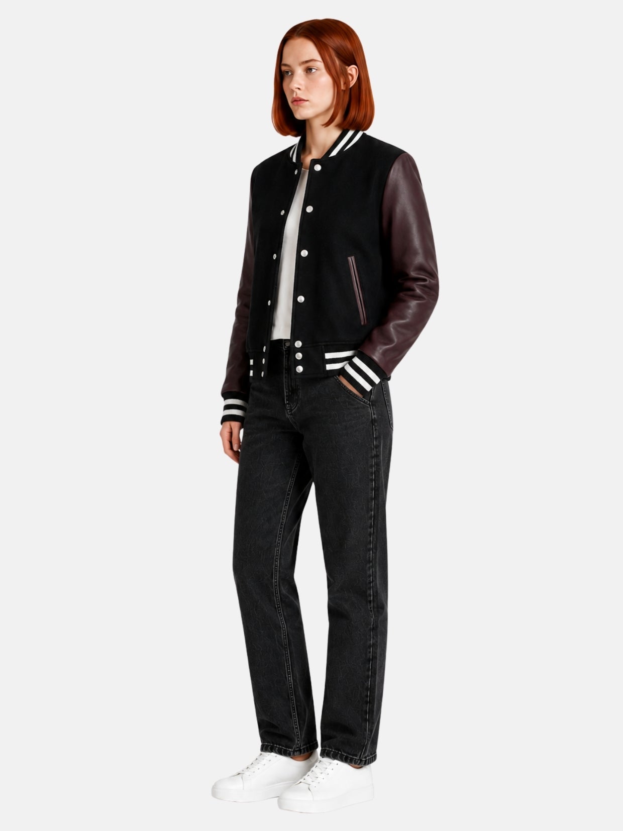 Full-length view of female model in black and burgundy varsity jacket with dark jeans