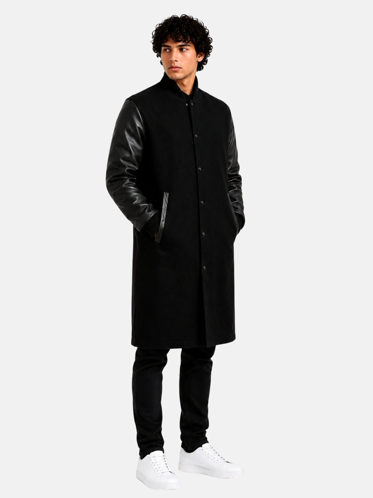 Model in long black wool varsity coat with top grain leather sleeves, hands in pockets